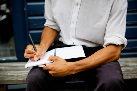 Un homme écrivant dans un carnet, illustrant le travail du style sur l’écriture.